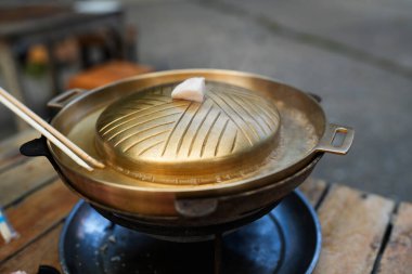 Pirinçten yapılmış barbekü tavası, tavanın üstünde domuz yağlı ekmek. Adı Moo ka ta. Tatillerde Taylandlılar arasında popüler bir yemek.