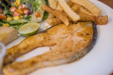 Bir tabak ızgara somon bifteği, salata ve patates kızartması. Kapat.