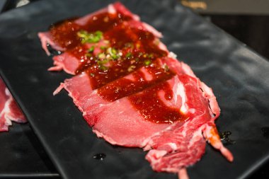 Shabu shabu yemeği için siyah tabakta ince dilimlenmiş çiğ et.
