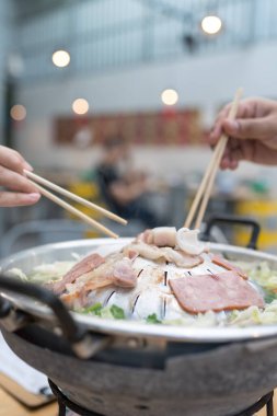 Mutlu arkadaş Tayland Barbeküsünün tadını çıkar. Adı Moo Kata. Adam yemek çubuklarını tavada dilimlenmiş domuz eti toplayıp çorbaya sebze koyuyor. Thai BBQ Mookata.