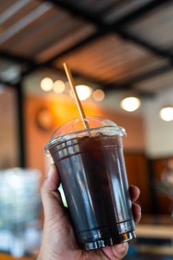 Kahve dükkanında şeffaf bir kahve bardağını buz gibi Amerikano ile tutarken..