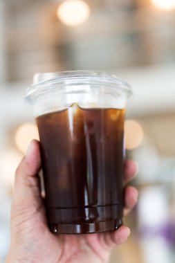 Elinde şeffaf kahve fincanı olan Amerikalı bir adam kahve dükkanının arka planında buz gibi soğuk tutuyor..