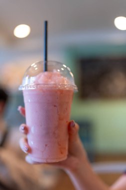 Kadın elinin üzerinde plastik bardakta çilekli smoothie.