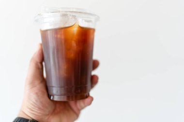 Beyaz arka planda, plastikten yapılmış soğuk bir Americano bardağı tutuyor.