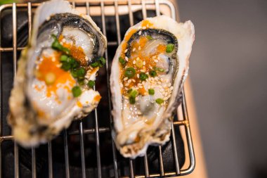 Balık yumurtası garnitürlü taze istiridye, üzerine beyaz susam ve ızgarada servis edilen taze soğan dilimi. Üst görünüm