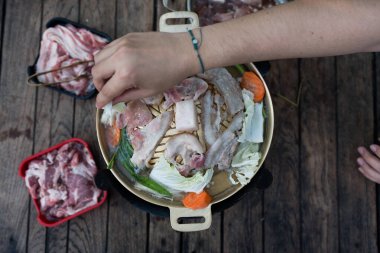 Adam tavaya çiğ sebze koyuyor, kızarmış tavaya domuz eti koyuyor, Tayland usulü barbekü yapıyor. Tatilde Taylandlılar. Izgara yemek tarzı domuz eti veya deniz bifteği ve haşlanmış sebze..