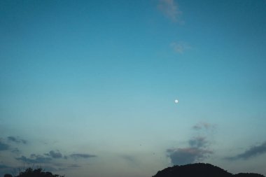 Mavi gökyüzüne karşı ayın küçük bir diski ve alacakaranlıkta bir dağ.