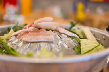 Cooking pork over a steaming Moo Kata grill, where sizzling meats and bubbling broth create a unique Thai BBQ experience