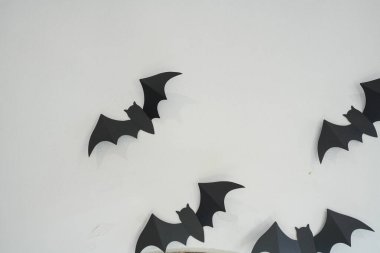 Black paper bats hanging against a cement white wall for halloween decoration display view