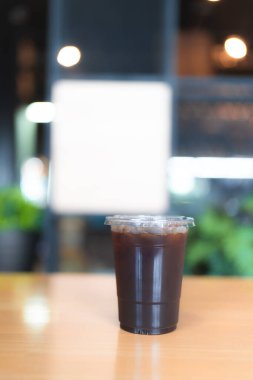 Buzlu Americano kahvesini cam bardakta, tahta masada plastik bardakta tazeliyorum.