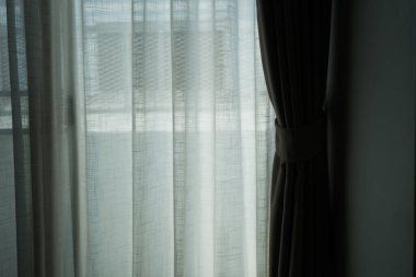 Saf perdeleri olan, rahat bir odada parlak bir pencere.