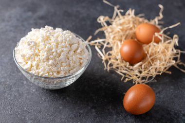 Cottage cheese in a glass bowl and eggs on the dark table, close-up, dairy products on table, sour cream, milk, cheese, eggs and yogurt.
