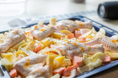 Çiğ tavuk budu, patates, soğan ve soslu havuç, otlar ve baharatlar bir kabın üzerinde, kapat..