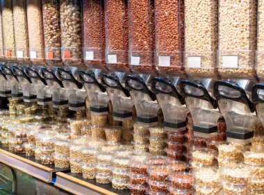 Dried nuts on the shelf at supermarket. Variety of seeds and nuts displayed in grocery store in reusable food dispensers. Shelf with glass jars full of dry food in organic shop. Grocery store interior.