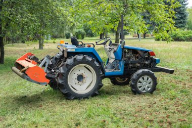 Elinde çim biçme makinesi olan mini traktör kuru çim biçiyor. Bölgenin bakımı, çimlerin biçilmesi, tarım makineleri.
