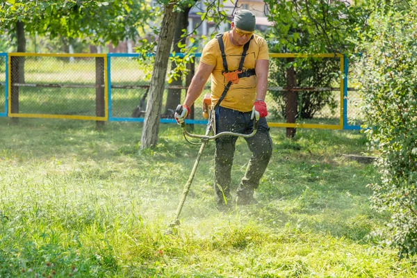 Adam benzin tırpanıyla çim biçiyor. Erkek bahçıvan, parkta elektrikli çim biçme makinesi ya da benzin ile çim biçiyor. Bahçe bakımı aletleri ve ekipmanları.