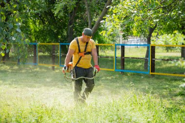 Adam benzin tırpanıyla çim biçiyor. Erkek bahçıvan, parkta elektrikli çim biçme makinesiyle çim biçiyor. Bahçe bakımı aletleri ve ekipmanları.