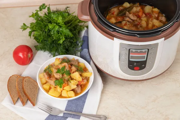 Beef, meat, stewed with potatoes, carrots, tomatoes and spices in modern multi cooker on kitchen table. Cooking stewed potatoes with meat in multicooker. Cooked dish. Copy space.
