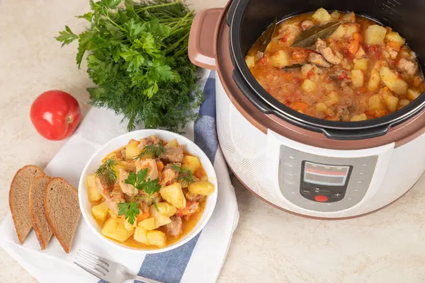 Beef, meat, stewed with potatoes, carrots, tomatoes and spices in modern multi cooker on kitchen table. Cooking stewed potatoes with meat in multicooker. Cooked dish. Copy space.