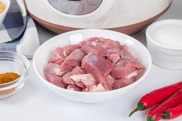 Prepared raw meat and other ingredients for cooking pilaf in modern multi cooker in kitchen on a table. Cooking pilau with meat in multicooker. Eastern cuisine.