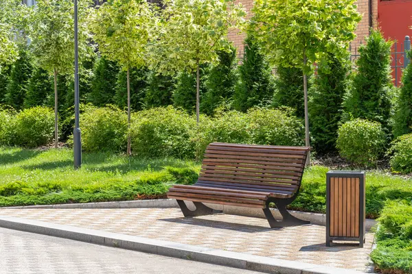 stock image Wooden bench in beautiful green city park or square at sunny day in spring or summer. City gardening concept. Environment improvement. Recreation area.