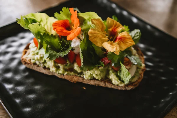 stock image Close up shot of avocado bruschetta with tomatoes and herbs. Morning tropical breakfast toast on black plate