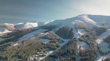 Slovakya 'nın Low Tatras dağlarındaki Demanovska Dolina köyünün yörüngesel kış manzarası. İnsansız hava aracı günbatımında karlı ve buzlu kozalaklı ormanlar arasında kayak merkezlerinin manzarası