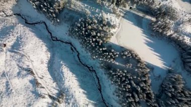 Slovakya 'daki alçak Tatras dağlarının kışın havadan görünüşü. İnsansız hava aracı günbatımında uzun gölgeli köknar ve çam ağaçlarının tepelerine, Demanovska Dolina köyündeki evler ve yollara bakıyor.