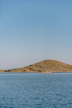 Açık mavi gökyüzü altında ufukta deniz suyu ve tepeler, Adriyatik Denizi, Hırvatistan 'daki Dugi Otok adası