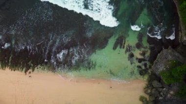 Kayalık önplanı, çarpan dalgaları ve yansıtan bir su kütlesi olan büyüleyici plajın havadan görünüşü. Dengesiz atmosfer, yakın çekim kayalar..