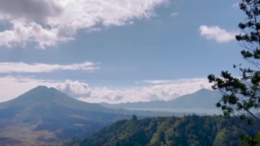 Bali 'de tropikal ağaçlar ve yapraklarla çevrili yeşil bir vadiyle birlikte bulutlu bir gökyüzünün altında manzaralı bir dağ manzarası. Huzurlu ve huzurlu doğal manzara