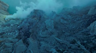 Ortasında gri bulutlar ve sisle çevrili bir krater deliği olan Ijen kayalık dağ volkanı manzarası.