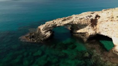 Kıbrıs 'ta Ayia Napa yakınlarında aşk köprüsü. Cavo Greco Ulusal Parkı 'ndaki kayalık hava manzarası, romantik turkuaz deniz dalgaları ve sudaki kayalardan kopan doğal köprü kemeri.