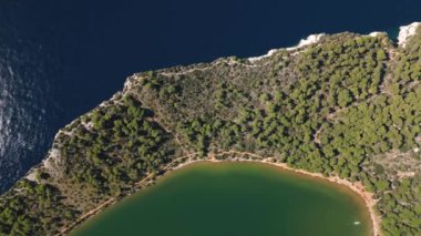 Hırvatistan 'ın Telascica Ulusal Parkı' ndaki Dugi Otok adasındaki deniz ve tuz gölü suları arasında yeşil ormanla kaplı kara parçasına insansız hava aracı manzarası