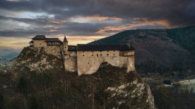 Slovakya 'daki ünlü Orava Kalesi Ortaçağ Oravsky Hrad' ının hava günbatımı panoramik görüntüsü. Şovalyelerin yüksek açılı manzarası kayaların üzerindeki kale dramatik bulutlu gökyüzü, akşam kuşları manzarası