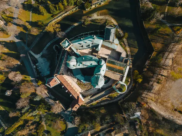 stock image Aerial top down view of Bojnicky Zamok in evening sunlight, famous castle in Bojnice, Slovakia. Overhead scene of medieval blue roofs and tree tops, road around fortress and long shadows of palace