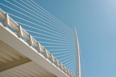 Modern köprü kablolarının açık mavi gökyüzüne yakın çekim. Görüntü, köprünün minimalist ve yapısal güzelliğinin vurgulandığı kusursuz çizgileri ve mühendislik detaylarını yakalıyor..
