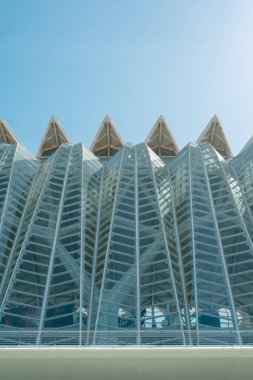 Karmaşık geometrik desenlere sahip yenilikçi cam yapı. Çağdaş tasarım, açık ve parlak bir gökyüzüne karşı belirlenmiş mühendislik ve modern mimari eğilimleri vurgular.