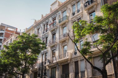 Çerçevesi yemyeşil ağaçlarla çevrili, karmaşık tasarımları olan tarihi bir binanın cephesi. Klasik mimari ve doğal elementlerin birleşimi şehir estetiğini geliştirir..