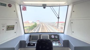 Modern bir tren kokpitinin iç görüntüsü, kontrol paneline ve ön pencere manzarasına odaklanıyor. Çağdaş tren sistemlerinin teknolojisini ve tasarımını vurgular.