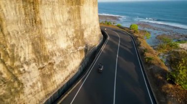 Bir motosiklet sürücüsü ile sahil yolu, takip eden bir kameradan görüntülendi. Yol, okyanus manzaralı bir uçurum boyunca esiyor, dinamik ve maceralı bir sahne yaratıyor..