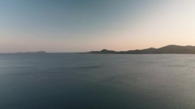 Sakin suları ve ufukta uzak adaları olan sakin kıyı manzarası. Sakin sahne, günbatımında huzur ve doğal güzelliği çağrıştırıyor..