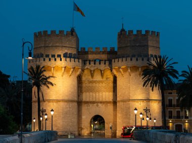 Valencia, İspanya 'daki Serranos Kuleleri' nin gece görüşü sokak lambalarıyla aydınlatılmış. Sahne, kulelerin ihtişamını ve tarihsel önemini yakalıyor..