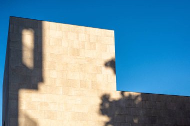 Açık mavi gökyüzüne uzanan gölgeli minimalist modern bina cephesi. Geometrik tasarım çağdaş mimari estetiği vurgular.