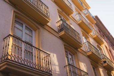 Valencia 'da birden fazla balkonu olan sıcak güneş ışığıyla yıkanmış bir binanın ön cephesi. Tekrarlanan şablonlar ve gölgeler görsel olarak çekici bir şehir manzarası yaratıyor..