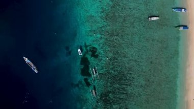 Yukarıdan bakıldığında, berrak sularda yüzen teknelerin görüntüsü, deniz tabanının detaylarını ortaya çıkarıyor. Sakin deniz manzarası, tropikal suların berraklığını ve güzelliğini vurguluyor.