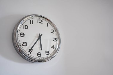 Round analog clock hanging on white wall. Shows clean and modern style with functional design. clipart