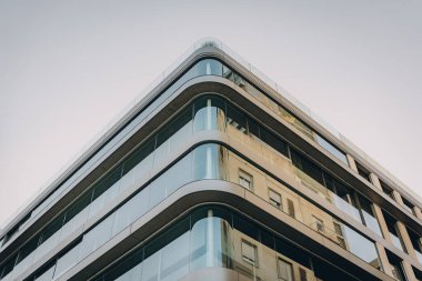 Yuvarlak kenarlı cam duvarlı ofis binası, kentsel bir alanda çağdaş mimari tarzda yer alıyor..