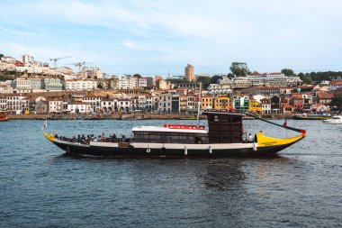 Turistlerle dolu klasik bir haham teknesi Douro Nehri boyunca yol alırken, arka planda Porto renkli nehir kenarı binaları bulunuyor. Porto, Portekiz - 11 Haziran 2025