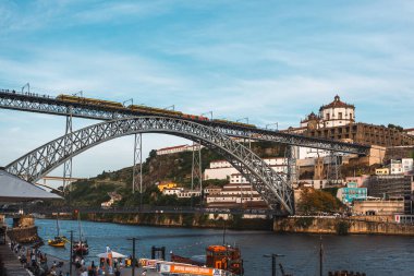İkonik Dom Luis Köprüsü, Douro Nehri üzerinde sarı tramvay geçidi, hareketli nehir kenarı etkinliği ve tarihi şehir manzarası. Porto, Portekiz - 11 Haziran 2025